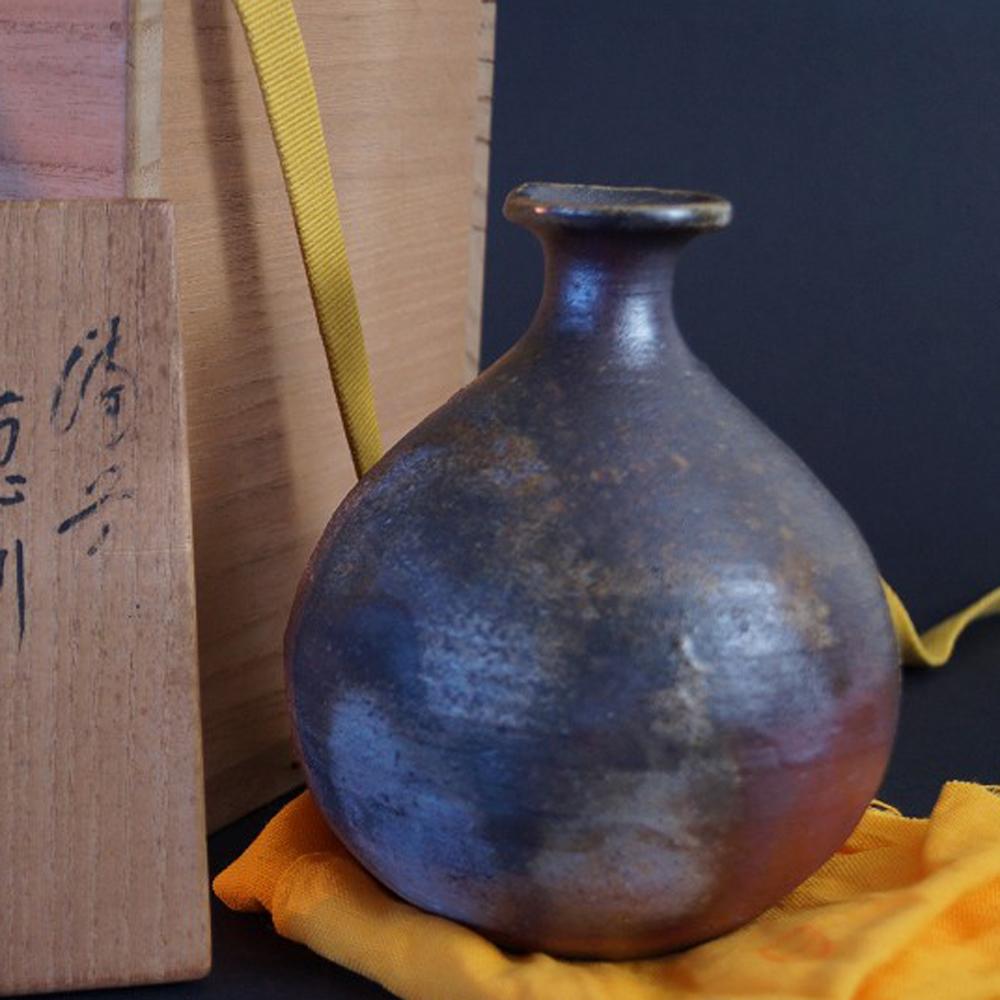 Aperçu gros plan du flacon à saké Bizen sur un tissu jaune avec la boîte de conservation